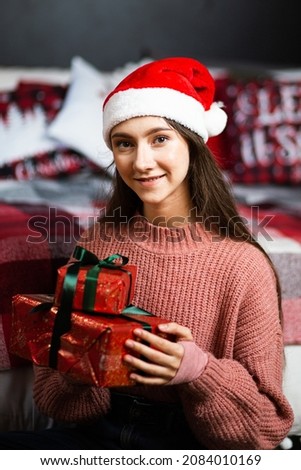 A girl in a Santa hat with gifts on the background of the New Year's interior.