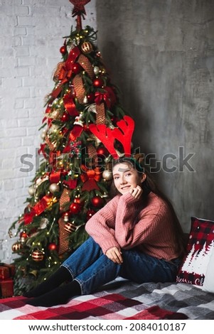 Girl with deer antlers on the background of the Christmas tree.