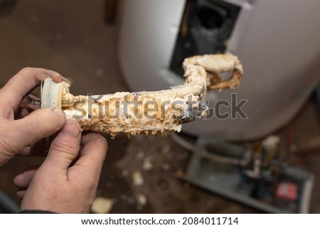 The plumber took it out of the boiler and holds in his hands the heating element coil, covered with limescale. Repair and maintenance, service of electric boilers. Royalty-Free Stock Photo #2084011714