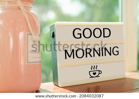 A sign with good morning letters is placed on a wooden table by the window in a cafe.