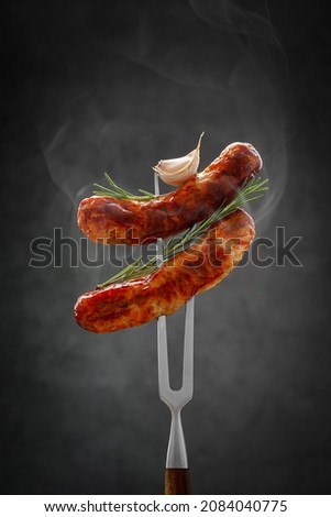 two fried hot thinking sausages on a meat fork with raspberry and garlic. grilled sausage, bbq concept Royalty-Free Stock Photo #2084040775