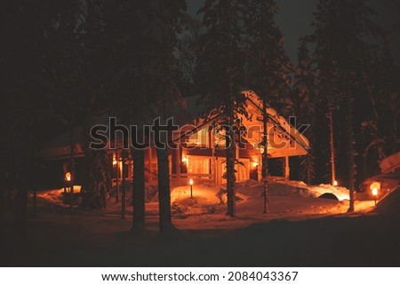 A view of cozy wooden scandinavian cabin cottage chalet house covered in snow near ski resort in winter with the christmas lights on, evening picture
