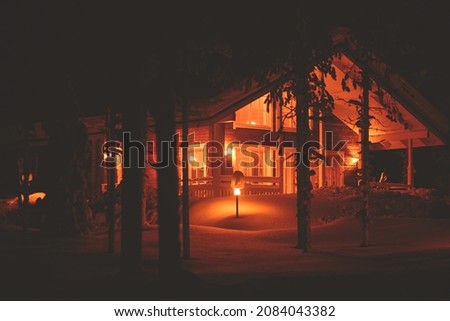 A view of cozy wooden scandinavian cabin cottage chalet house covered in snow near ski resort in winter with the christmas lights on, evening picture
