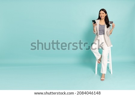 Young Asian businesswoman sitting and showing credit card for making payment in mobile phone isolated on green background Royalty-Free Stock Photo #2084046148