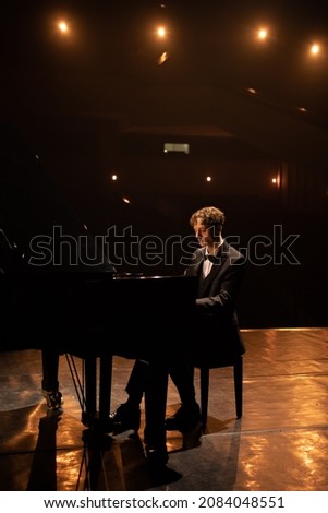 Young 20s aspiring musician playing grand piano on a stage of a huge concert hall