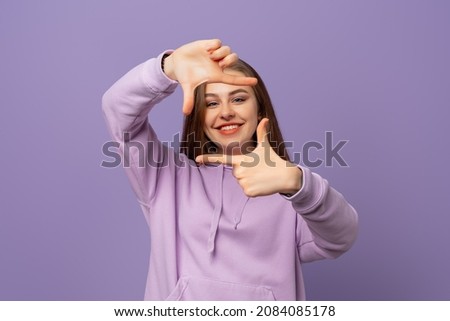 Young brunette woman making frame with hands and fingers with happy face over purple background. Looking at camera. Positive emotions concept
