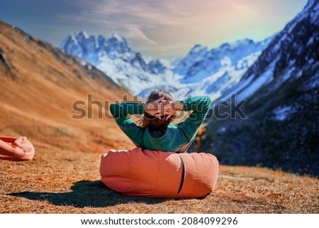 Wanderer girl sitting on soft chair during resting in a camping. Traveler enjoying scenic landscape while traveling in a mountain valley Royalty-Free Stock Photo #2084099296