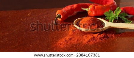 Red paprika seasoning in wooden spoon side view next to peppercorns on wooden red cracked background