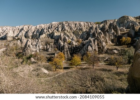 Goreme National Park and the Rock Sites of Cappadocia, Goreme. Volcanic landscape – UNESCO World Heritage Site. Autumn yellow trees, hills, mountains, cave houses.