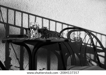 A table, a glass, a chair and shadows on the wall. Black and white photography.