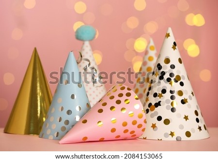 Beautiful party hats on pink table against blurred festive lights