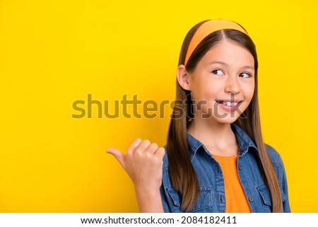 Photo of funky dreamy student girl wear denim shirt smiling looking pointing thumb up back empty space isolated yellow color background