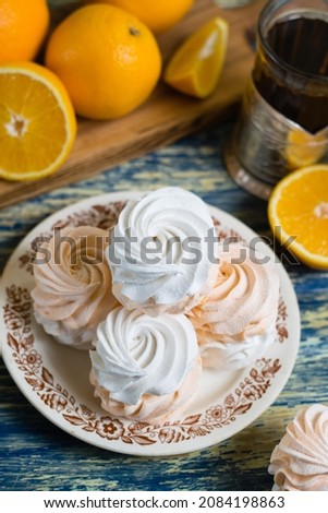 Delicious marshmallow with orange filling in a vintage plate, sliced orange on a cutting board and tea in a glass