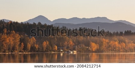 Amazing autumn landscape of a forest and mountains by a river in morning sunlight. Colorful trees reflected in a water. Beautiful outdoor autumnal landscape. Travel photo, selective focus