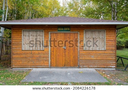 A building with brown log siding and a sign with the words social center hung over double wood doors. The sign is green with yellow lettering and references a clubhouse for elderly or aged people.