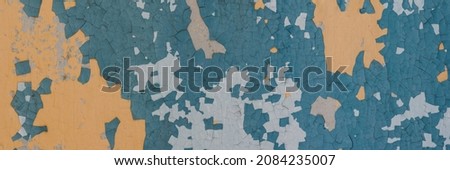 Peeling paint on the wall. Panorama of a concrete wall with old cracked flaking paint. Weathered rough painted surface with patterns of cracks and peeling. Wide panoramic grungy texture for background Royalty-Free Stock Photo #2084235007