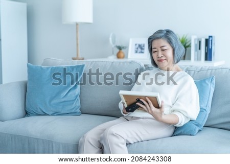 Asian Senior woman looks family photographs with gentle in living room. Loving beautiful elderly older female grandmother sitting on sofa enjoy retirement life, missing husband and relative in house.