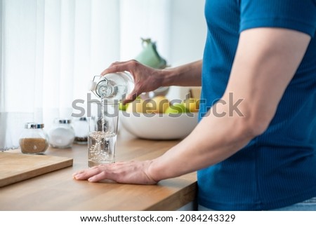 Close up hands of active strong man pouring clean water into glass. Attractive thirsty male drink or take a sip of mineral natural in cup after wake up for health and wellbeing in kitchen in house. Royalty-Free Stock Photo #2084243329