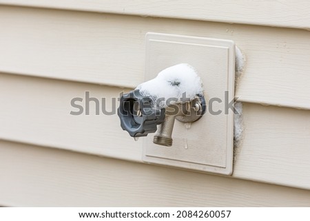 Outdoor water spigot covering in snow during winter. Home repair, maintenance and weatherproofing concept. Royalty-Free Stock Photo #2084260057
