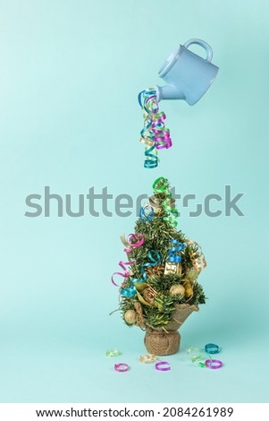 A multicolored streamer flowing from a floating watering can onto a Christmas tree. The minimum concept of the New Year. Contemporary art. Place for text.