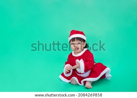 Christmas santa santy, Baby in santa claus cloth. Asian happy baby smiling, sitting on green background. Cute 1 year baby laughing with copy space as Christmas, santa, santy or christmas festival.