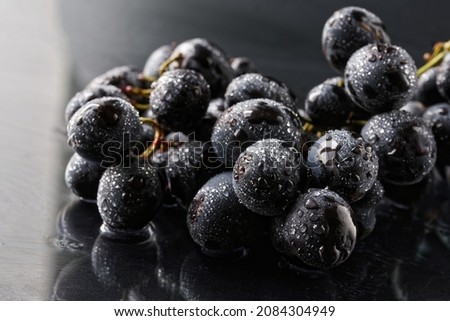 Black grapes covered with moisture droplets on a reflective surface. Macro. Selective focusing. Close-up