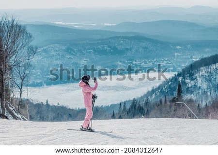 Woman taking photo on ski vacation using phone - Woman skier using phone app on ski trail slope taking pictures of amazing winter nature landscape. Girl using mobile smartphone in awesome ski wear.