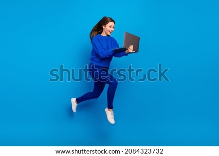 Full length body size view of attractive cheerful trendy girl jumping using laptop blogging isolated on bright blue color background