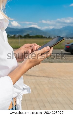 Women's hands hold a mobile phone against the background of mountains, car close-up on a sunny day. Vertical photo