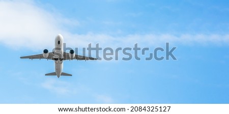 Low-flying white passenger plane with landing gear on a background of blue sky with clouds with copy space, bottom view. Plane took off and hides the landing gear in flight. Banner Royalty-Free Stock Photo #2084325127