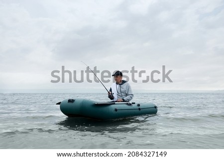 Man fishing with rod from inflatable rubber boat on river