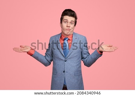 Funny clueless male entrepreneur in suit shrugging shoulders and expressing misunderstanding on pink background in studio while looking at camera