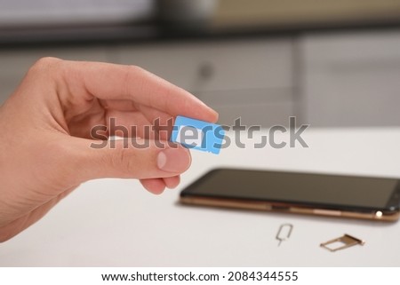 Woman with SIM card at white table indoors, closeup