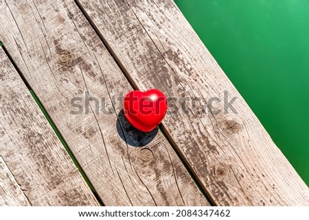 The red heart lies on a wooden pier on the lake. Beautiful summer concept of a serene holiday.