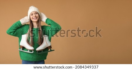 Beautiful young woman with ice skates and winter clothes on color background with space for text
