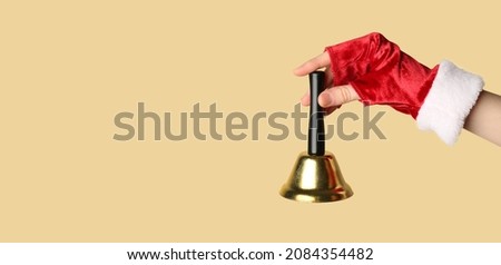 Female hand in mitten holding golden Christmas bell on color background with space for text