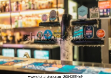 Defocused or blurry of bottles Of Alcohol And Spirits On Backlight Shelves At A Pub Or Bar with tap beers. Drink shelf of a restaurant full of bottles in raw with a warm and modern back light