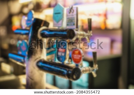 Defocused or blurry of bottles Of Alcohol And Spirits On Backlight Shelves At A Pub Or Bar with tap beers. Drink shelf of a restaurant full of bottles in raw with a warm and modern back light