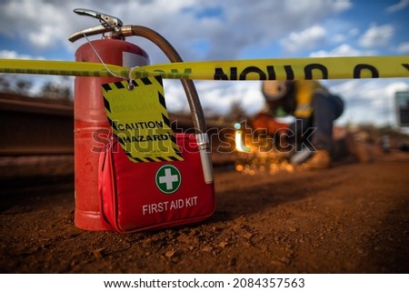 Safety workplace yellow striped caution tape warning sign barricade exclusion zone preventing from public access first aid kit with fire extinguisher defocused construction worker using oxy hot work   Royalty-Free Stock Photo #2084357563