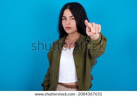 Cheerful european girl wearing trendy clothes standing over blue background  indicates happily at you, chooses to compete, has positive expression, makes choice.