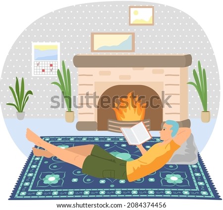 Cute man reading literature. Book lover concept with young man lying relax on floor near fireplace and reading magazine. Concept of homeward and comfort. Person relaxes after work in his apartment Royalty-Free Stock Photo #2084374456