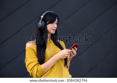 Attractive and beautiful Caucasian brunette girl in headphones listening to music in headphones and using a smartphone over a black background.