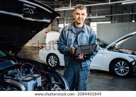 Portrait of positive friendly car mechanic using a computer laptop to diagnosing and checking up on car engines parts for fixing and repair. Royalty-Free Stock Photo #2084401849