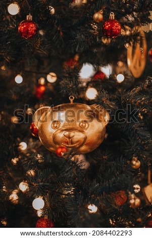 Golden shiny Christmas toy bear head and red Christmas balls hanging on the Christmas tree. New Year's details in the festive atmosphere
