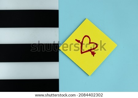 On a blue background with a striped part there is a sticker on which a heart is drawn. A declaration of love. Office supplies. Valentine's day.