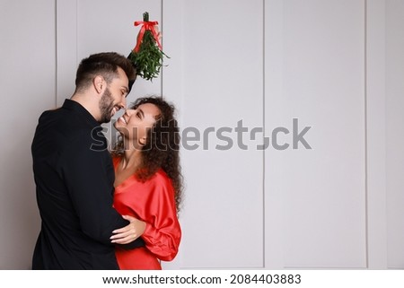 Lovely couple under mistletoe bunch near light grey wall. Space for text