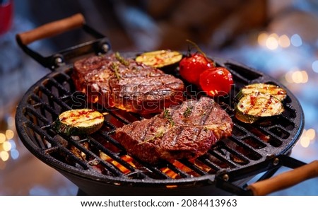 High angle of delectable beef steaks placed near zucchini and tomatoes being grilled on barbecue grid Royalty-Free Stock Photo #2084413963