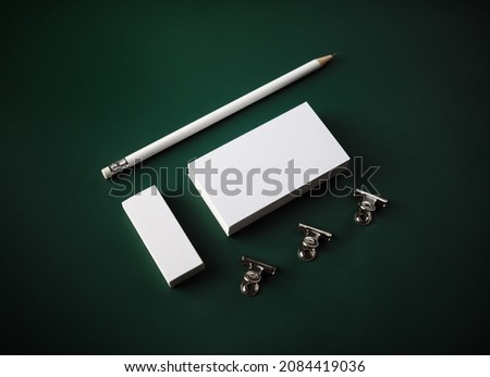 Photo of blank stationery. Blank business card, pencil, eraser and clips on green background.