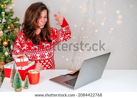 A young woman in a red sweater uses a laptop during the Christmas holidays and New Year. The concept of online shopping and communication