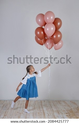 Teenager girl with pigtails with pink balloons in a blue sundress in the interior.
